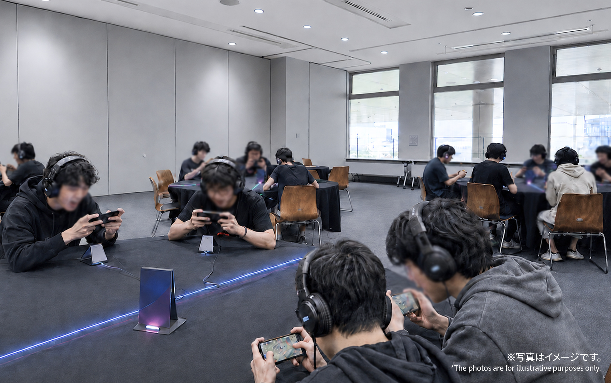 セミナールームでの予選のイメージ。円卓にプレーヤーが着座し、スマートフォンゲームでの試合に集中している。