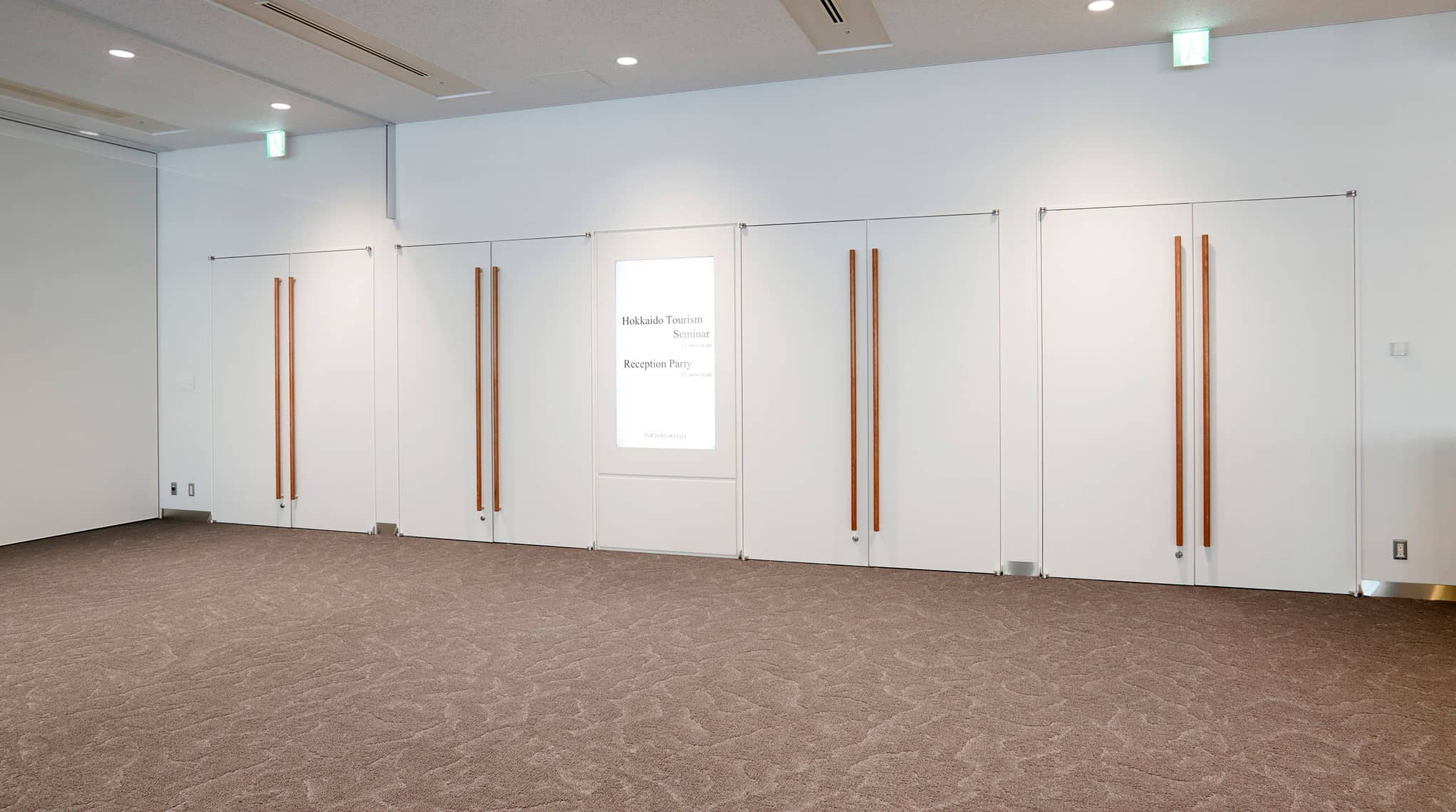 廊下へ続く4つの両開きドアと、ドア中央のデジタルサイネージの様子