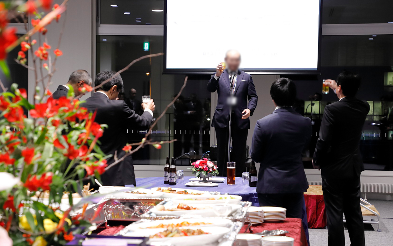 男性が壇上に上がり会場で乾杯の挨拶をしている様子